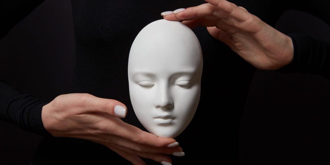 White plaster mask face is holding woman's fingers on a black background, copy space. Concept social psychological masks