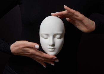 White plaster mask face is holding woman's fingers on a black background, copy space. Concept social psychological masks
