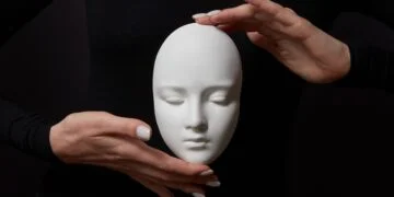White plaster mask face is holding woman's fingers on a black background, copy space. Concept social psychological masks