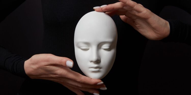 White plaster mask face is holding woman's fingers on a black background, copy space. Concept social psychological masks